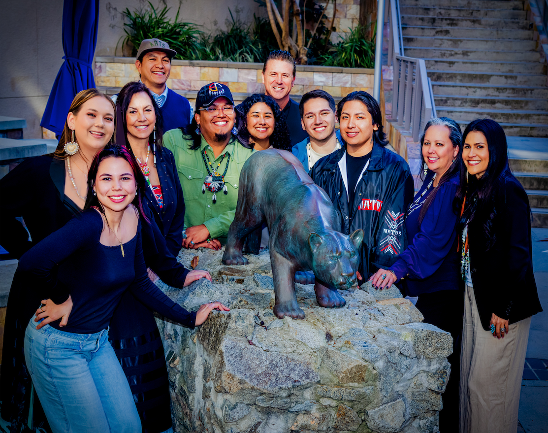 Native American students and faculty posed outside around a small statue of a CSUSM cougar on a pedestal